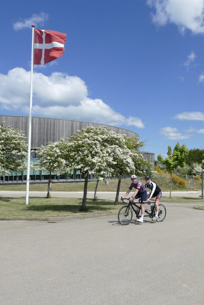 Glade cyklister med dansk flag i baggrunden